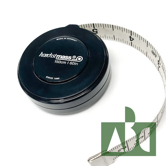 Product photo of a retractable tape measure in a black, round plastic case. Text printed on the case reads 